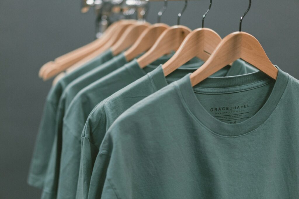 A row of green t-shirts hanging on wooden hangers